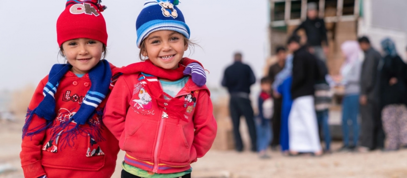 2 Syrian children smile at camera after receiving winter clothing kits from UNICEF and its partner Mateen.