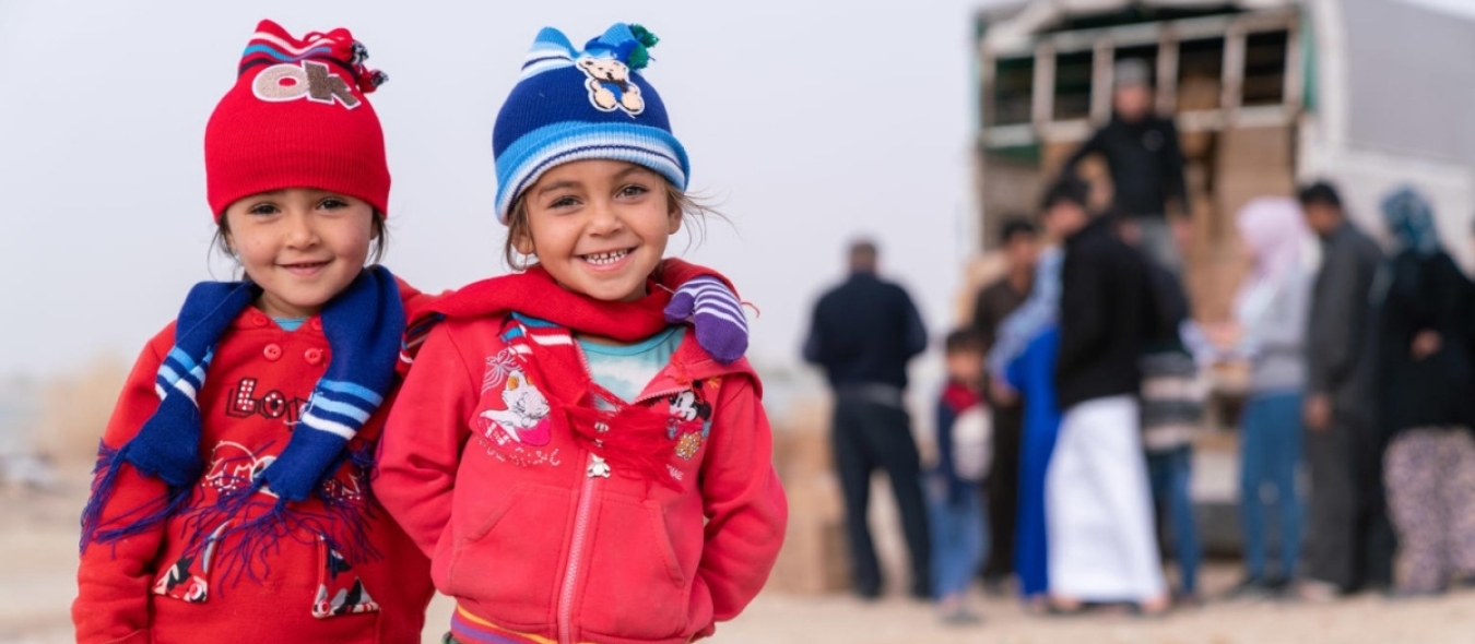 2 enfants syriens sourient à la caméra après avoir reçu des kits de vêtements d'hiver de l'UNICEF et de son partenaire Mateen.