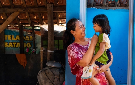 Mother holds her 3-year-old daughter in front of a newly constructed toilet in their home. 