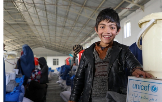 Child smiles next to a UNICEF winterization kit in Afghanistan.