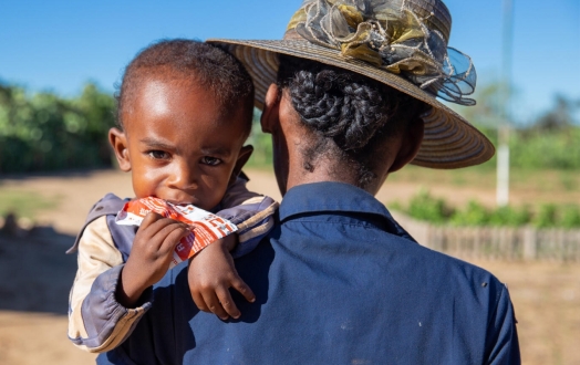 Mother carries her 2-year-old son while he eats ready-to-use therapeutic food (RUTF).
