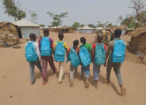 Group of boys carry UNICEF backpacks and walk towards thatch huts and tent shelters in an area of the Gado site for refugees from the Central African Republic.