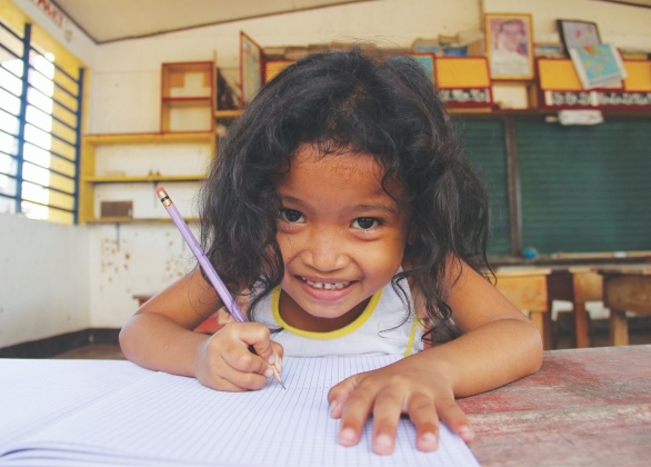 5-year-old girl sits with notebook and pencil inside a school building partly damaged by the typhoon Haiyan in coastal village of Cogon, Palo, Leyte.