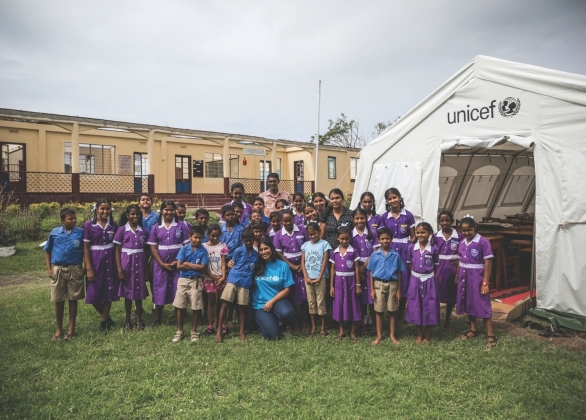 Students and their teachers stand in front of a UNICEF-provided school tent.
