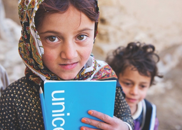 A girl holds school essentials: a pencil and textbook.