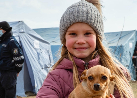 A refugee child from Ukraine stands with her dog at a Temporary Refugee Center.
