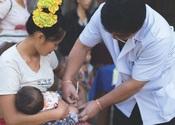 A baby, held by their mother, receives a tetanus shot from a health care provider.