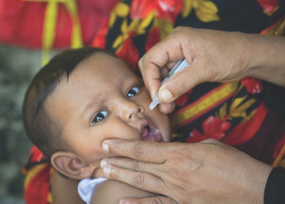 A health worker feeds an OPV vaccination drop to a young child.