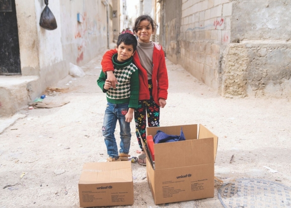 A brother and sister stand beside a UNICEF box of winter clothing in Jordan.