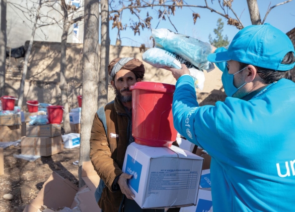 A UNICEF volunteer gives a stack of emergency supplies to a man.