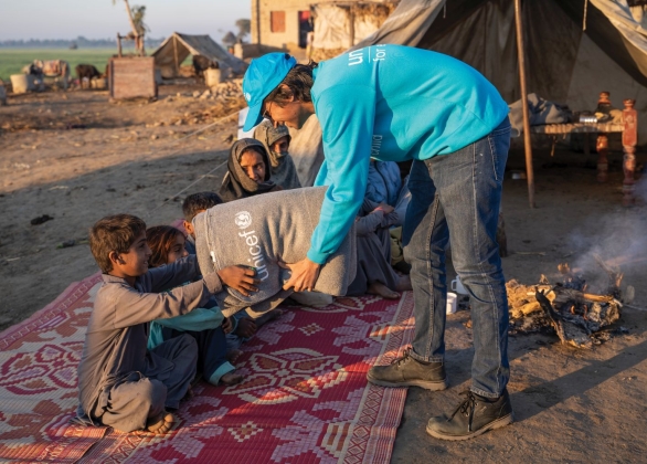 Des enfants reçoivent des couvertures de secours d’un bénévole de l’UNICEF.