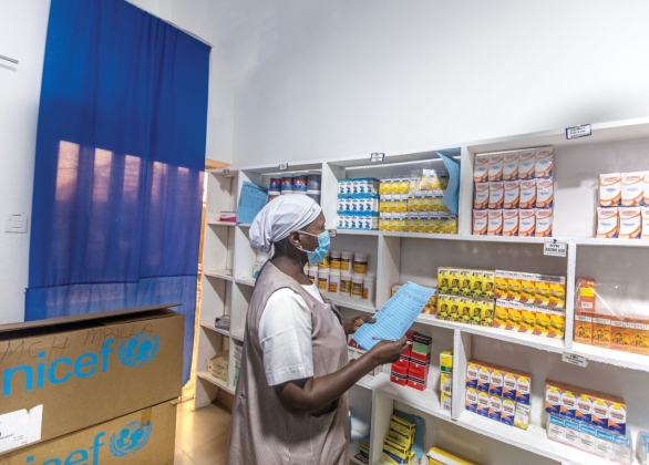 A staff member holds a list and checks shelves of healthcare supplies.