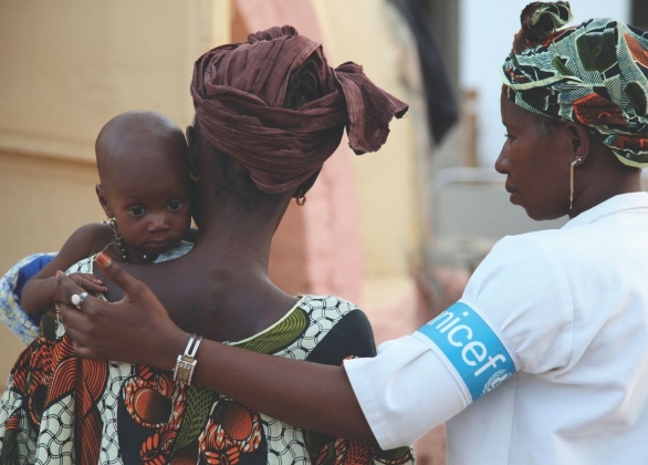 UNICEF aid worker puts her arm around mother and baby.
